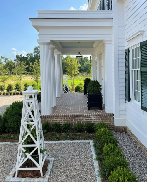 A white house with columns, a lantern, and landscaped greenery along a brick pathway.