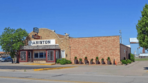 Exterior of the Ariston building, featuring a brick facade and signage, with trees and clear blue sky in the background.