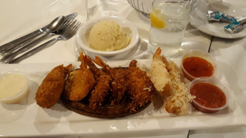 A plate of fried shrimp with dipping sauces, a side of mashed potatoes, and a glass of water with lemon.