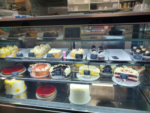 A display case filled with various cakes and cupcakes, featuring colorful decorations and labels.