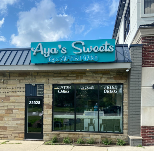 Exterior of Aya's Sweets shop featuring a sign and large windows displaying custom cakes, ice cream, and fried Oreos.