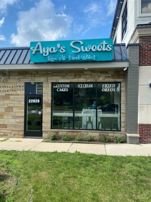 Exterior of Aya's Sweets shop featuring a sign and large windows displaying offerings like custom cakes and ice cream.