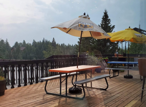 Outdoor seating area with colorful umbrellas overlooking a forested landscape and a body of water.