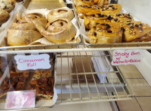 A display case with cinnamon rolls and sticky buns with walnuts and raisins, labeled on pink signs.