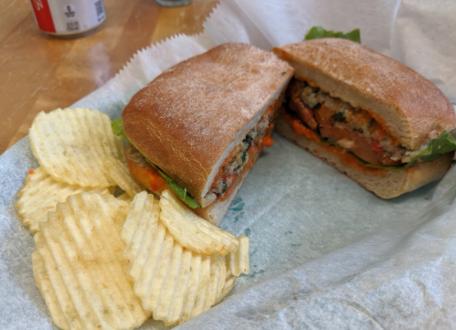 A sandwich with lettuce and a filling, served with a side of ridged potato chips on a paper wrapper.