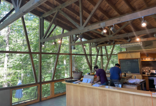 Two people prepare food in a modern kitchen with large windows overlooking a forested area.