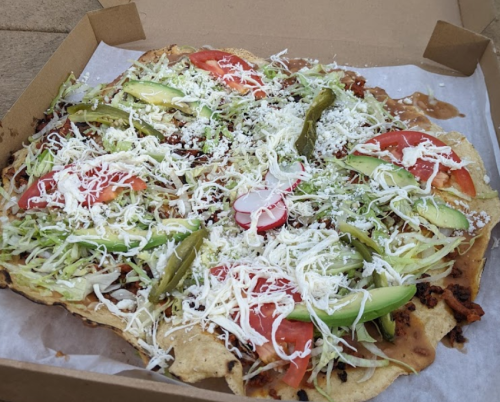 A large, colorful nacho platter topped with lettuce, tomatoes, radishes, avocado, jalapeños, and shredded cheese.