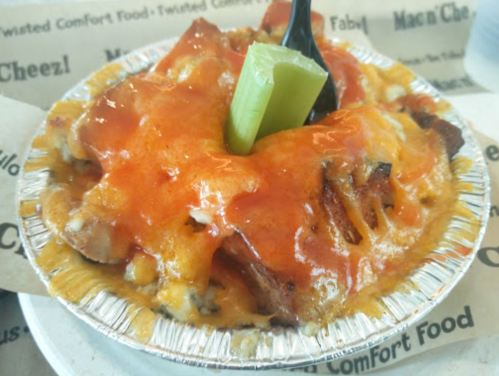 A close-up of a cheesy mac and cheese dish topped with barbecue meat, drizzled with sauce, and garnished with celery.