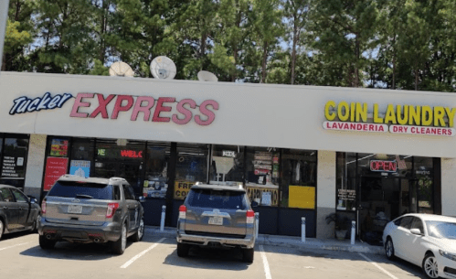 A storefront featuring "Tucker Express" and "Coin Laundry" signs, with parked cars in front and trees in the background.