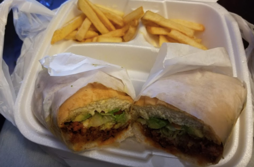 A takeout container with a cut sandwich filled with lettuce and a side of golden French fries.
