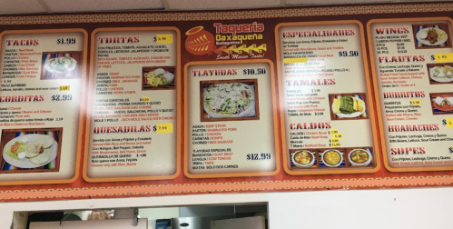 Menu board from Taqueria Oaxaqueña featuring tacos, tortas, quesadillas, wings, tamales, and more with prices listed.