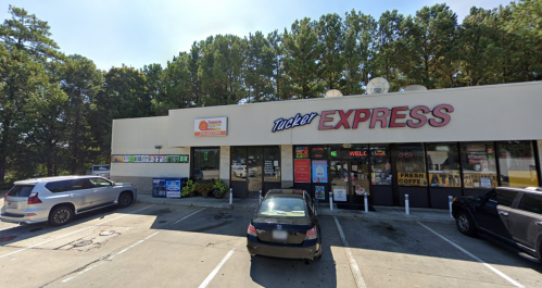 A convenience store named Tucker Express with a parking lot, surrounded by trees and several parked cars.