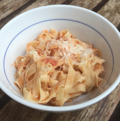 A bowl of fettuccine pasta topped with grated cheese and a light tomato sauce.