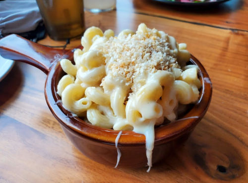 A bowl of creamy macaroni and cheese topped with breadcrumbs, served on a wooden table.