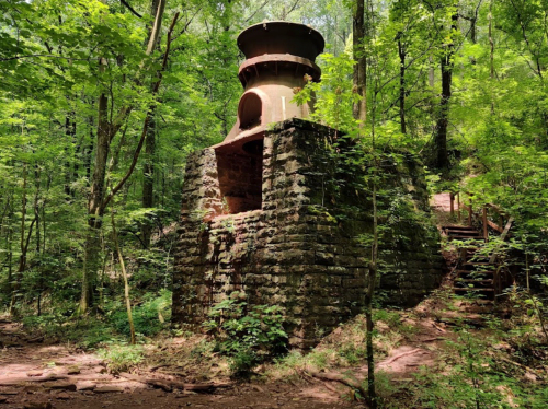 Abandoned stone structure surrounded by lush green trees in a forested area.