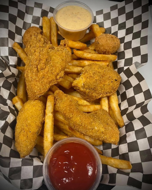 A basket of golden fried chicken tenders and fries, served with ketchup and a dipping sauce.