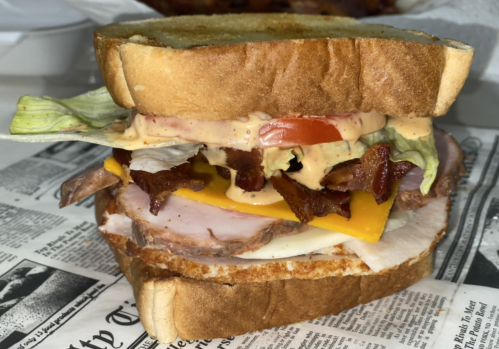 A stacked sandwich with layers of meats, cheese, lettuce, tomato, and sauce, served on toasted bread.