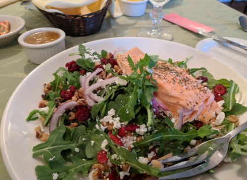 A fresh salad with arugula, salmon, red onions, walnuts, and cranberries, served on a white plate.