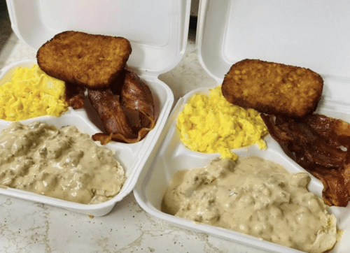 Two takeout containers with scrambled eggs, bacon, hash browns, and sausage gravy.