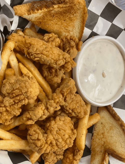 A basket of golden fried chicken pieces, crispy fries, and two slices of toasted bread, served with a side of dipping sauce.