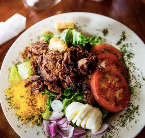 A colorful salad with shredded meat, lettuce, tomatoes, cheese, onions, and croutons on a white plate.
