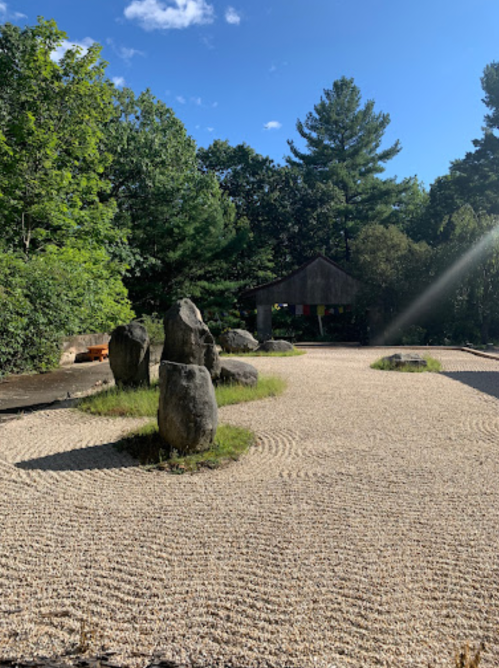 A serene outdoor space featuring large rocks, raked gravel, and lush greenery under a clear blue sky.