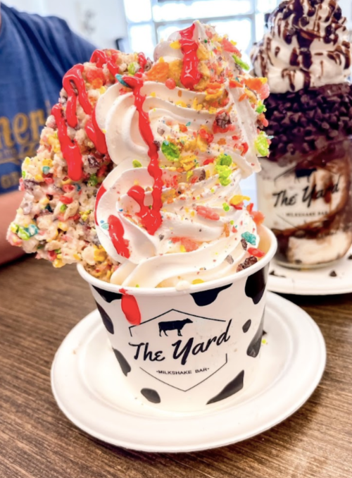 A large swirl of soft serve ice cream topped with colorful cereal and red drizzle in a cup from The Yard Milkshake Bar.
