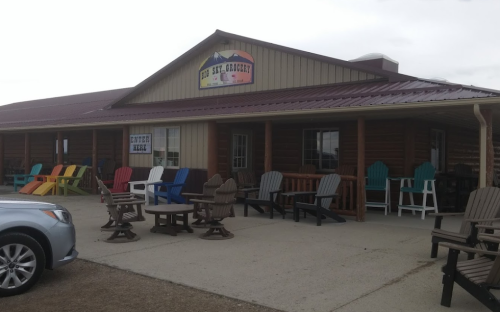 A rustic building with a metal roof, featuring colorful outdoor chairs and a sign that reads "Eat, Set, Go!"