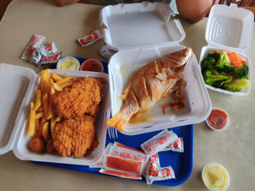 A tray with fried fish, chicken tenders, fries, broccoli, and various dipping sauces in takeout containers.