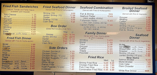 Menu board featuring various fried fish sandwiches, seafood dinners, side orders, and family meal options with prices.