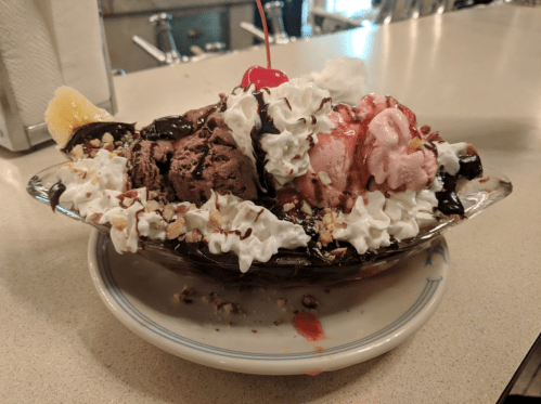 A colorful ice cream sundae topped with whipped cream, nuts, a cherry, and chocolate syrup in a glass dish.