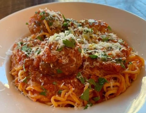 A plate of spaghetti topped with meatballs, marinara sauce, grated cheese, and fresh herbs.
