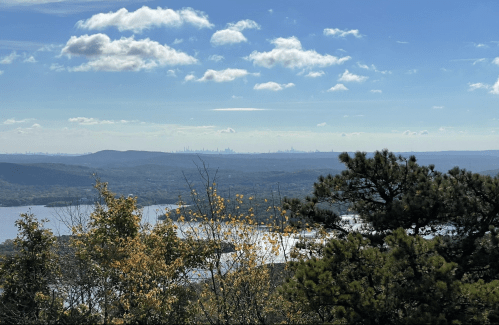 A scenic view of rolling hills, a lake, and distant city skyline under a blue sky with scattered clouds.