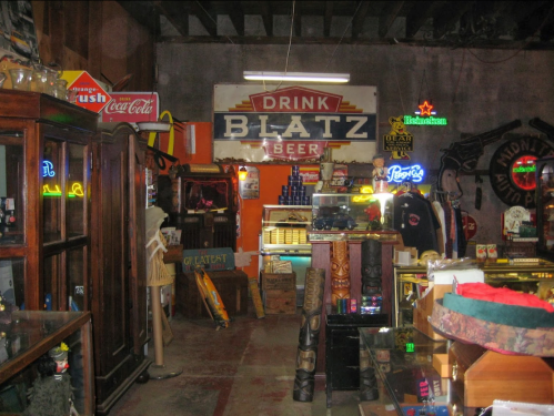 A vintage shop interior featuring various memorabilia, neon signs, and a prominent "Drink Blatz Beer" sign.