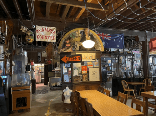 Interior of a rustic restaurant with wooden tables, vintage decor, and various flags hanging from the ceiling.