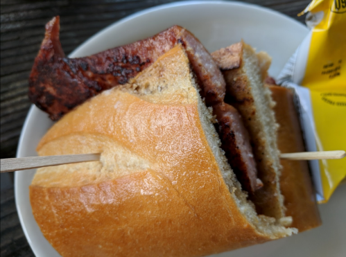 A close-up of a sandwich with sliced meat on a soft bun, held together with a wooden skewer.