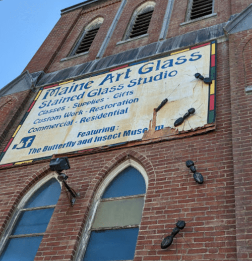 Sign for Maine Art Glass Stained Glass Studio on a brick building, featuring classes, supplies, and a museum.