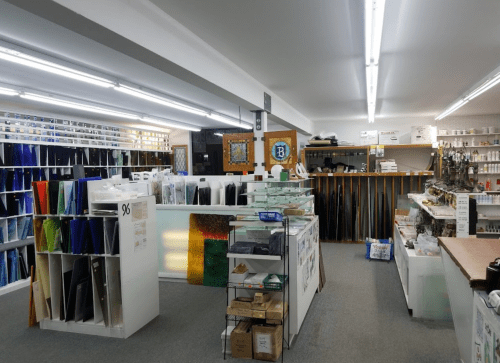 A well-organized store interior with shelves of colorful glass, tools, and supplies for crafting or home improvement.
