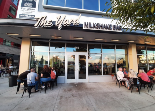 Exterior of The Yard Milkshake Bar with people seated outside, enjoying milkshakes on a sunny day.