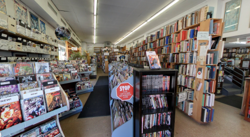 A cozy bookstore interior filled with shelves of books, magazines, and a display stand in the center.