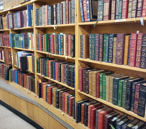 A wooden bookshelf filled with colorful, vintage leather-bound books arranged neatly in rows.