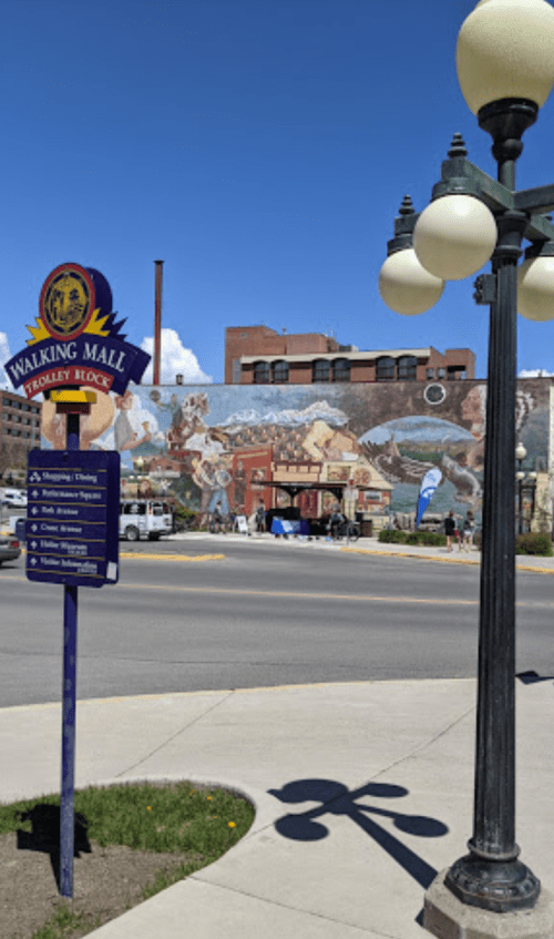 A sign for a walking mall with a colorful mural in the background and a blue sky above.