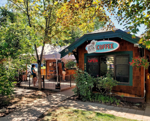A cozy coffee shop with a sign reading "Coffee" and outdoor seating surrounded by trees and greenery.