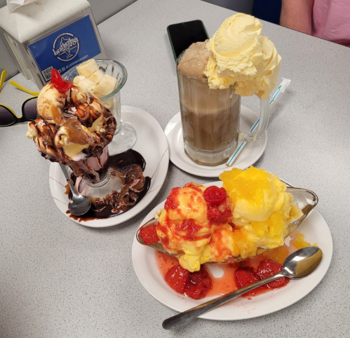 Three colorful desserts on a table: a chocolate sundae, a root beer float, and a fruit-topped ice cream dish.