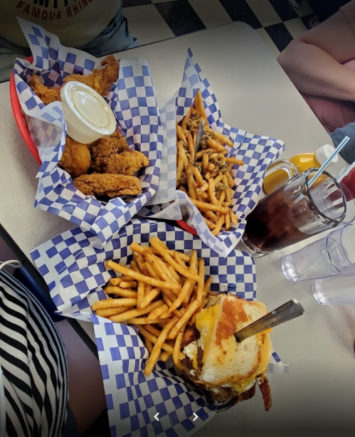 A table with two baskets of fries, fried chicken, and a burger with cheese, accompanied by drinks in glasses.