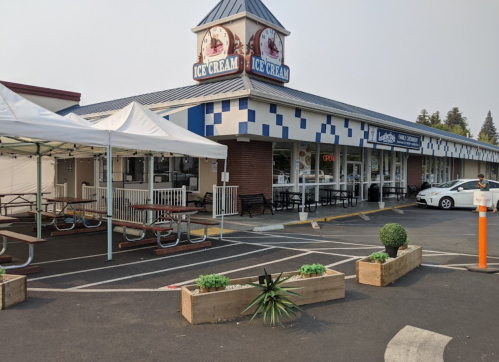 A storefront with an "Ice Cream" sign, outdoor seating, and a tent, set in a parking lot.