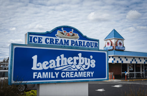 Sign for Leatherby's Family Creamery, featuring "Ice Cream Parlour" with a blue and white design, under a cloudy sky.