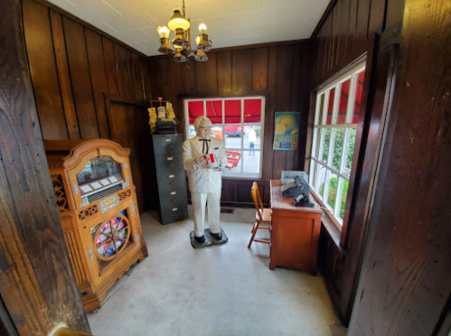 A vintage room featuring a statue of a man in a suit, a jukebox, a desk, and wooden paneling.