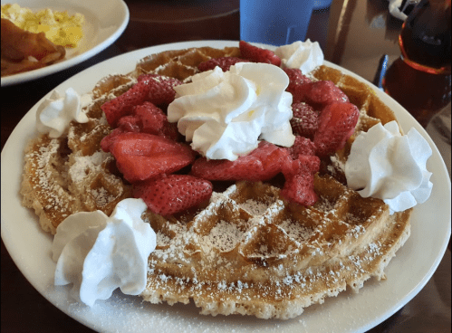 A golden waffle topped with whipped cream and fresh strawberries, served on a white plate.