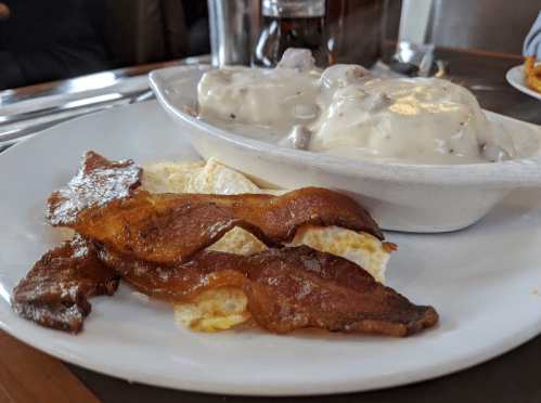 A plate with crispy bacon, eggs, and biscuits topped with creamy sausage gravy.
